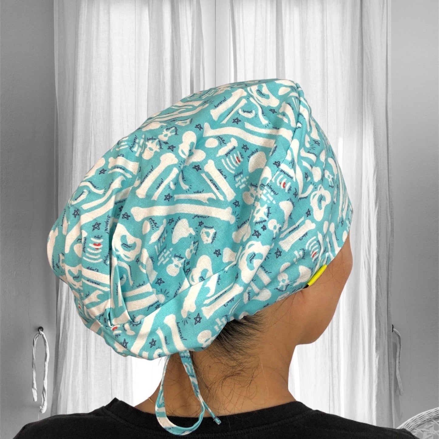 A scrub cap made from teal fabric featuring a pattern of white dental-themed icons, including teeth, bones, and dental tools.