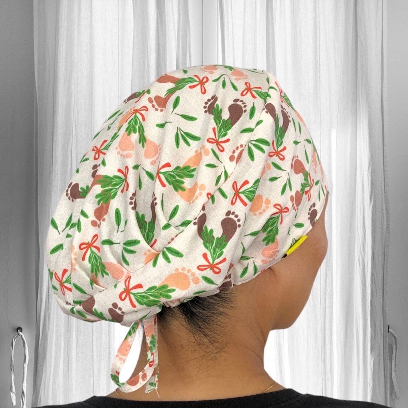 A person wearing a colorful scrub cap, featuring a pattern of footprints, leaves, and red bows.