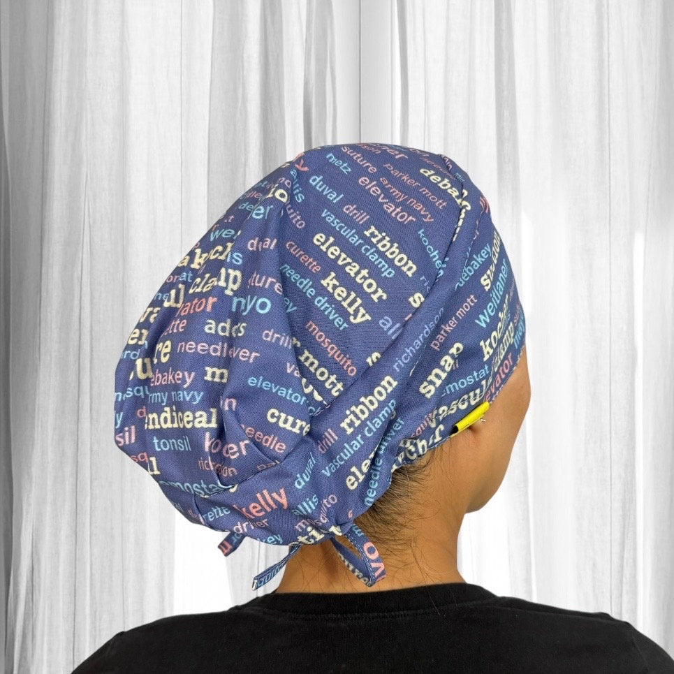 A person wearing a scrub cap featuring a colorful pattern of medical instruments and terms such as "elevator," "clamp," and "needle."