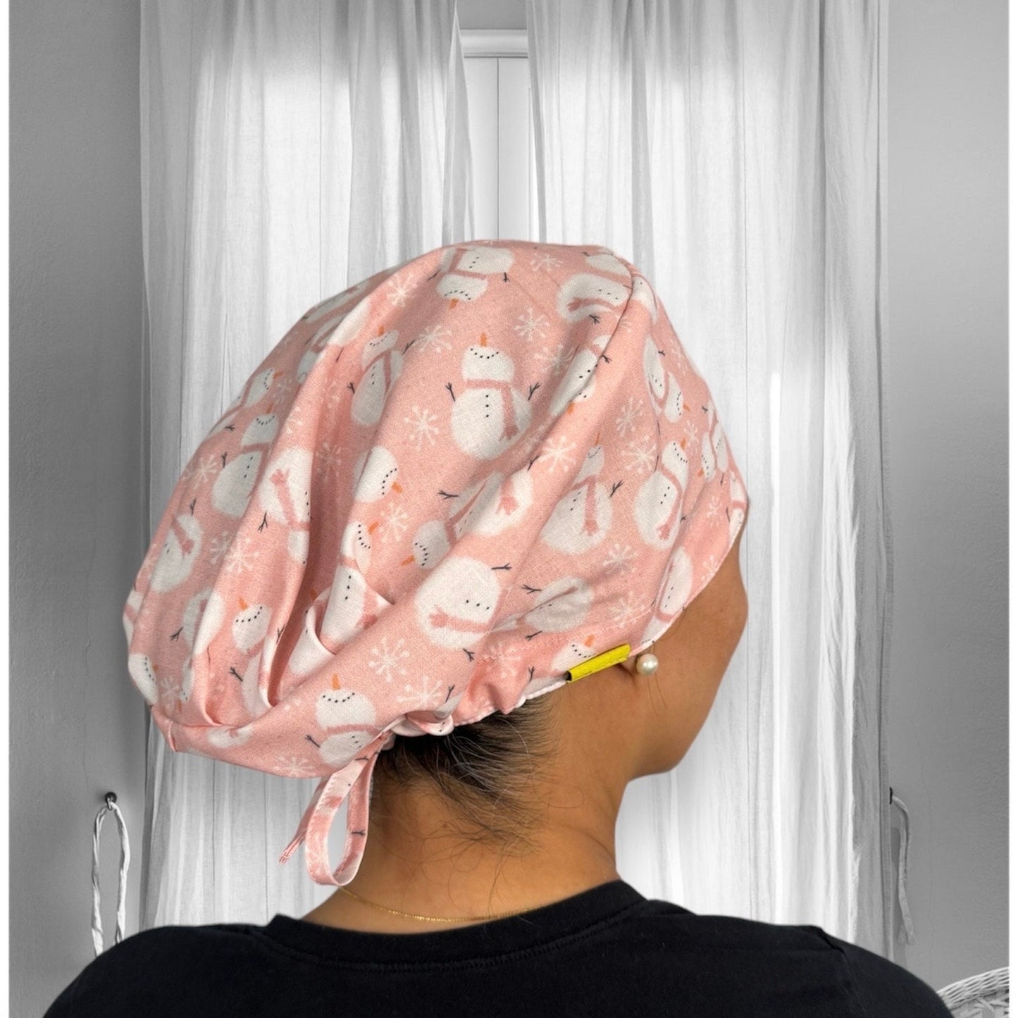 A person wearing a pink scrub cap with a pattern of snowmen and snowflakes.