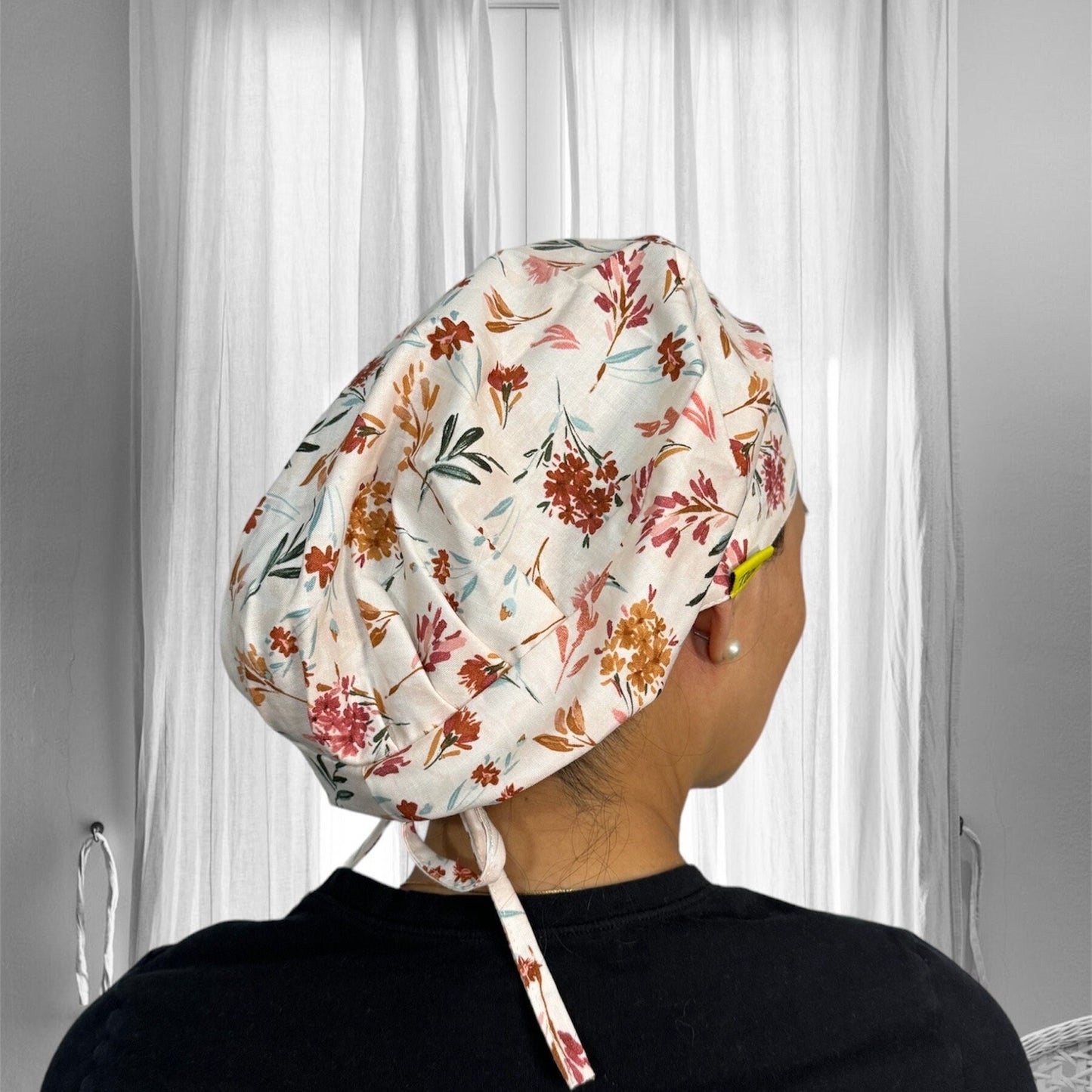 A floral-patterned scrub cap tied at the back, with vibrant orange, pink, and green flowers against a light background.