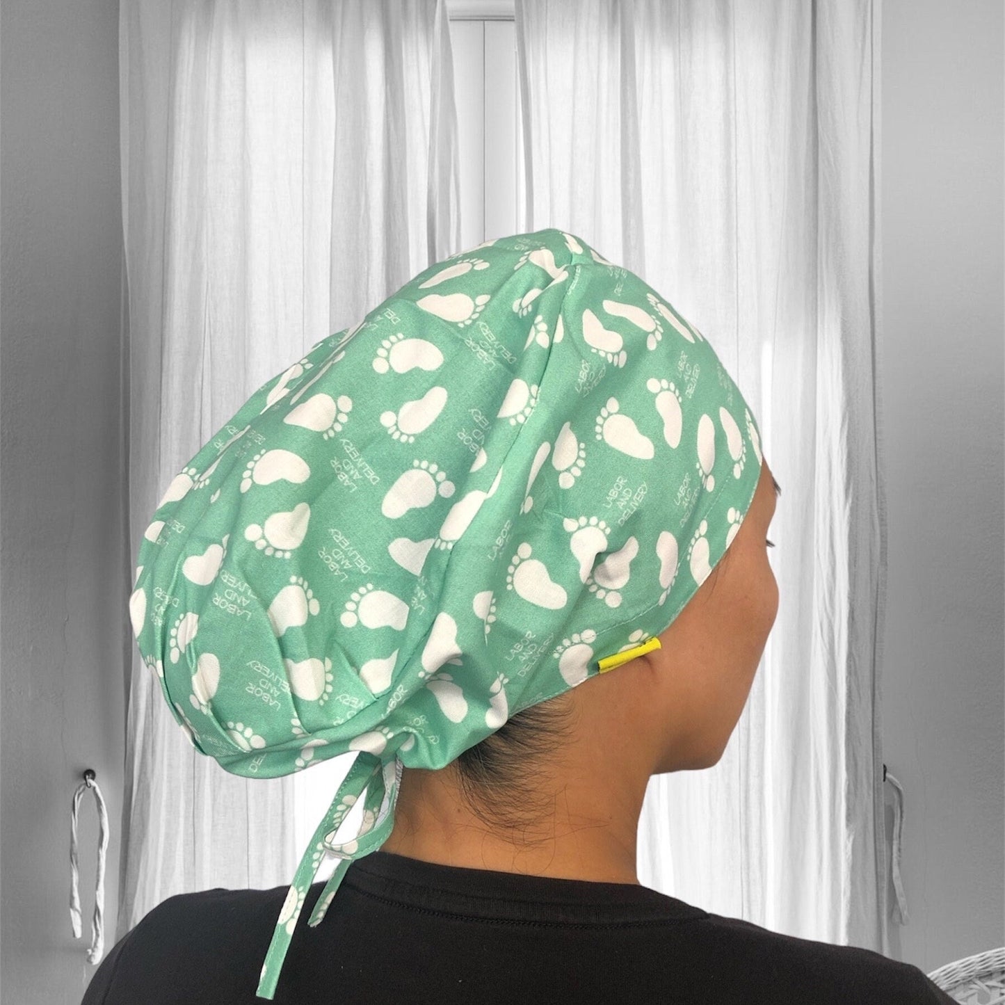 A green scrub cap with a pattern of white baby footprints.