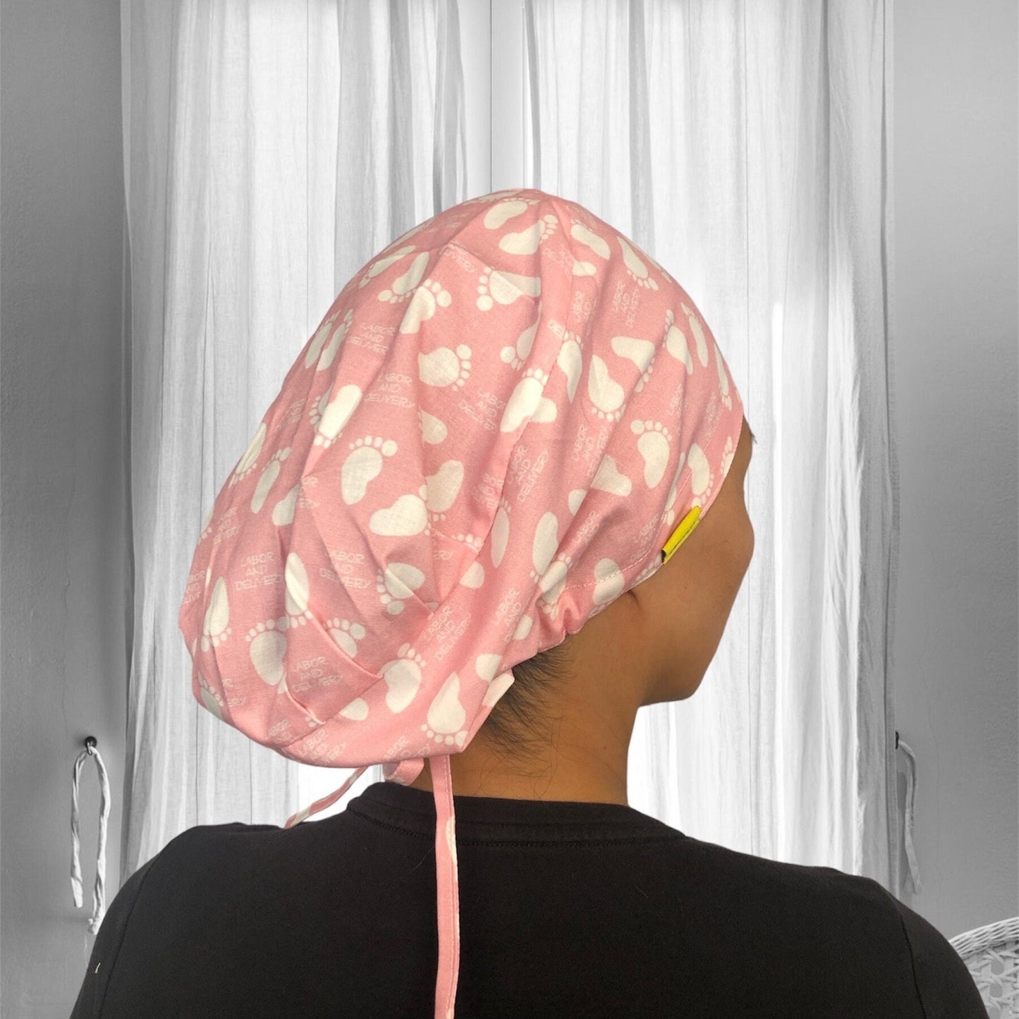 A pink scrub cap with a pattern of white baby footprints.