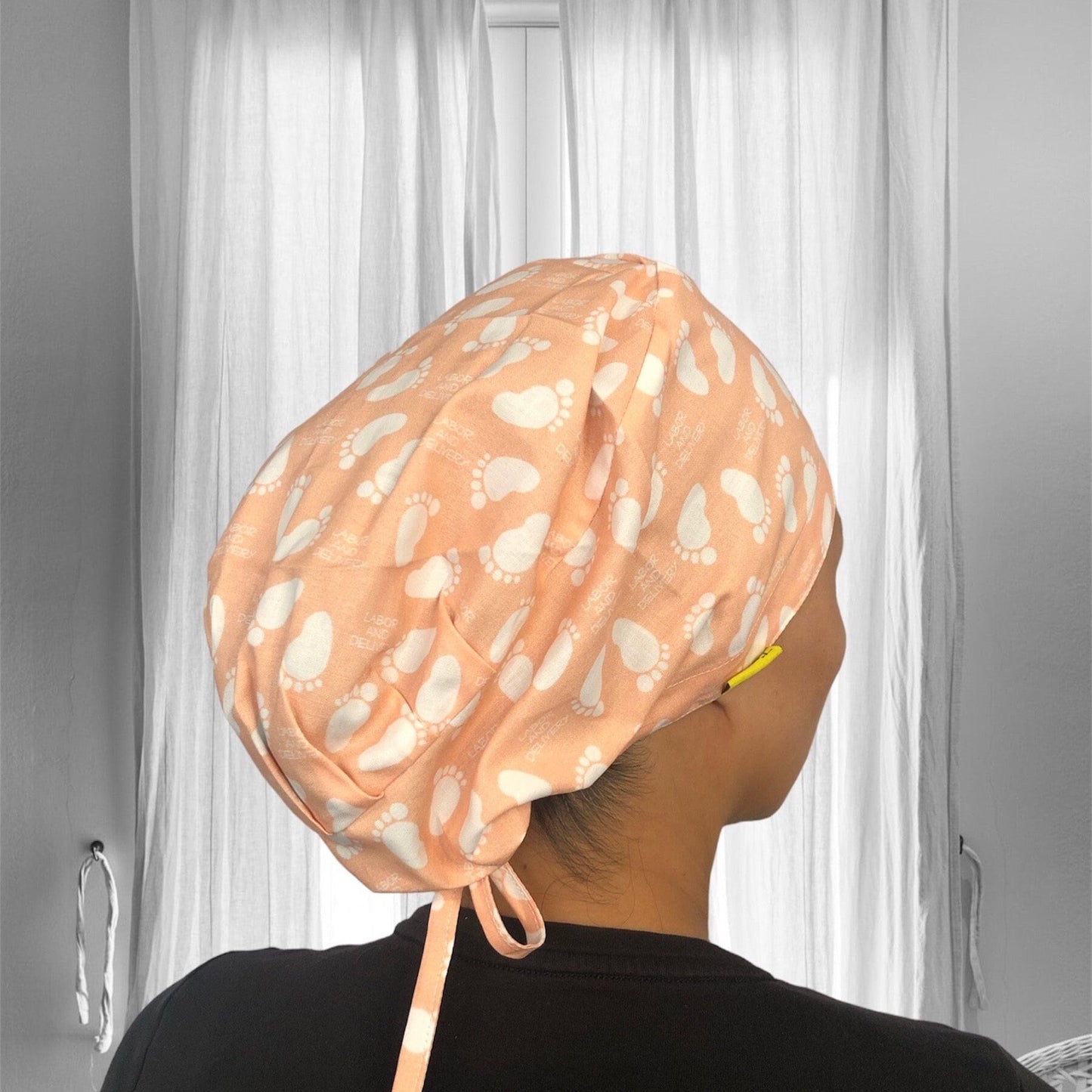 A peach scrub cap with a pattern of white baby footprints.