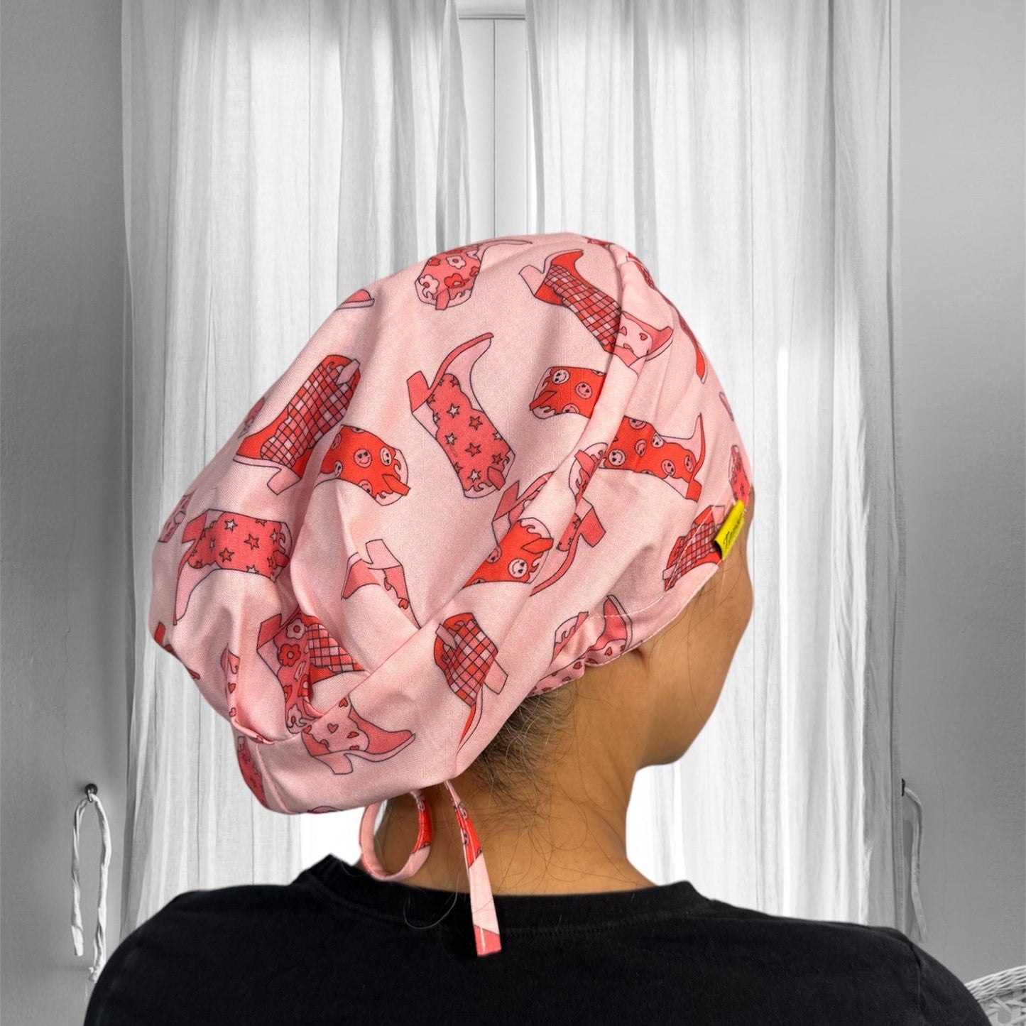 A person wearing a pink scrub cap with playful red dog patterns. The cap is securely tied at the back.