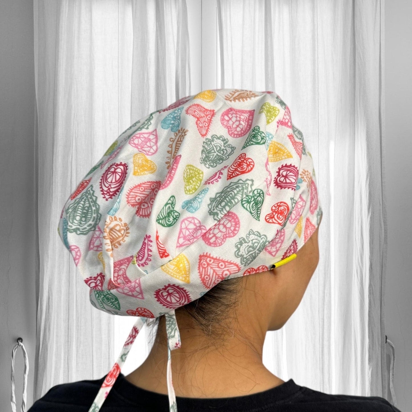 A colorful scrub cap with vibrant geometric and floral patterns. The cap's design features a variety of intricate motifs in shades of red, green, yellow, and orange.