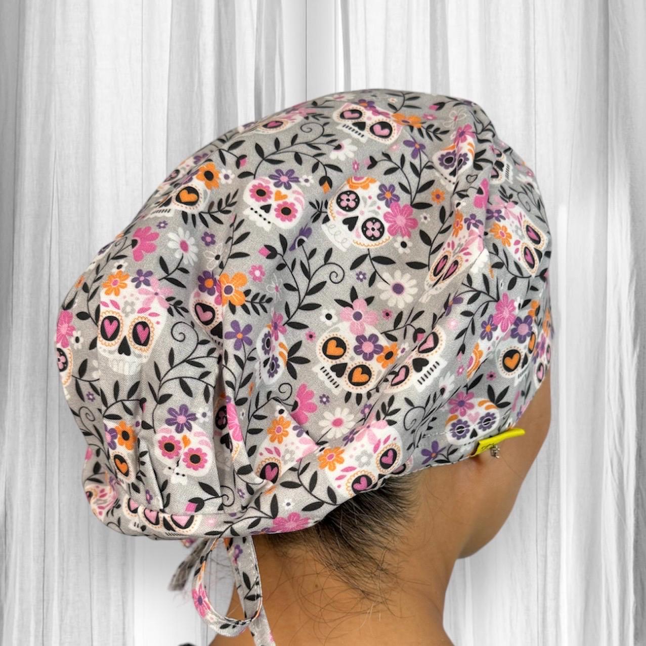 A colorful scrub cap featuring a lively pattern of sugar skulls and vibrant flowers in shades of pink, orange, and purple.
