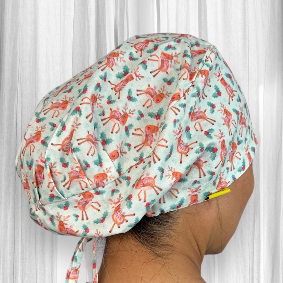 A colorful scrub cap featuring a festive design with adorable reindeer patterns on a light background.
