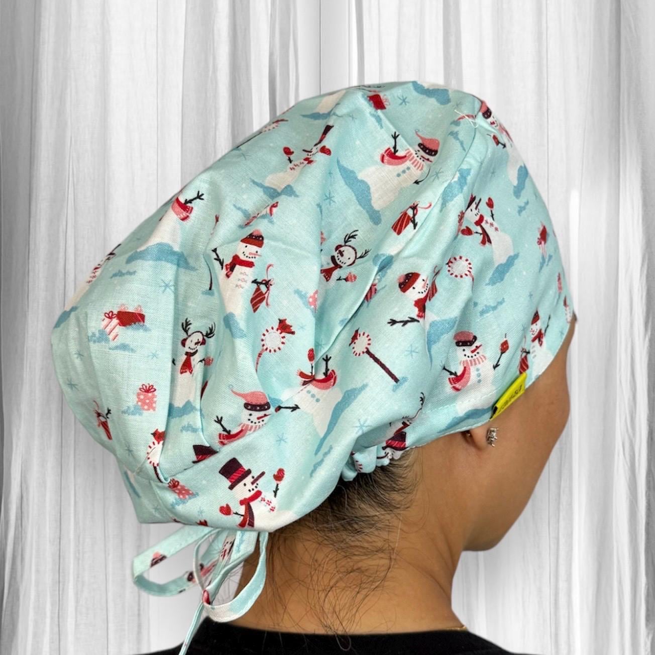 A person wearing a light blue scrub cap featuring a festive pattern. The design includes snowmen, candy canes, and snowflakes in red and white.