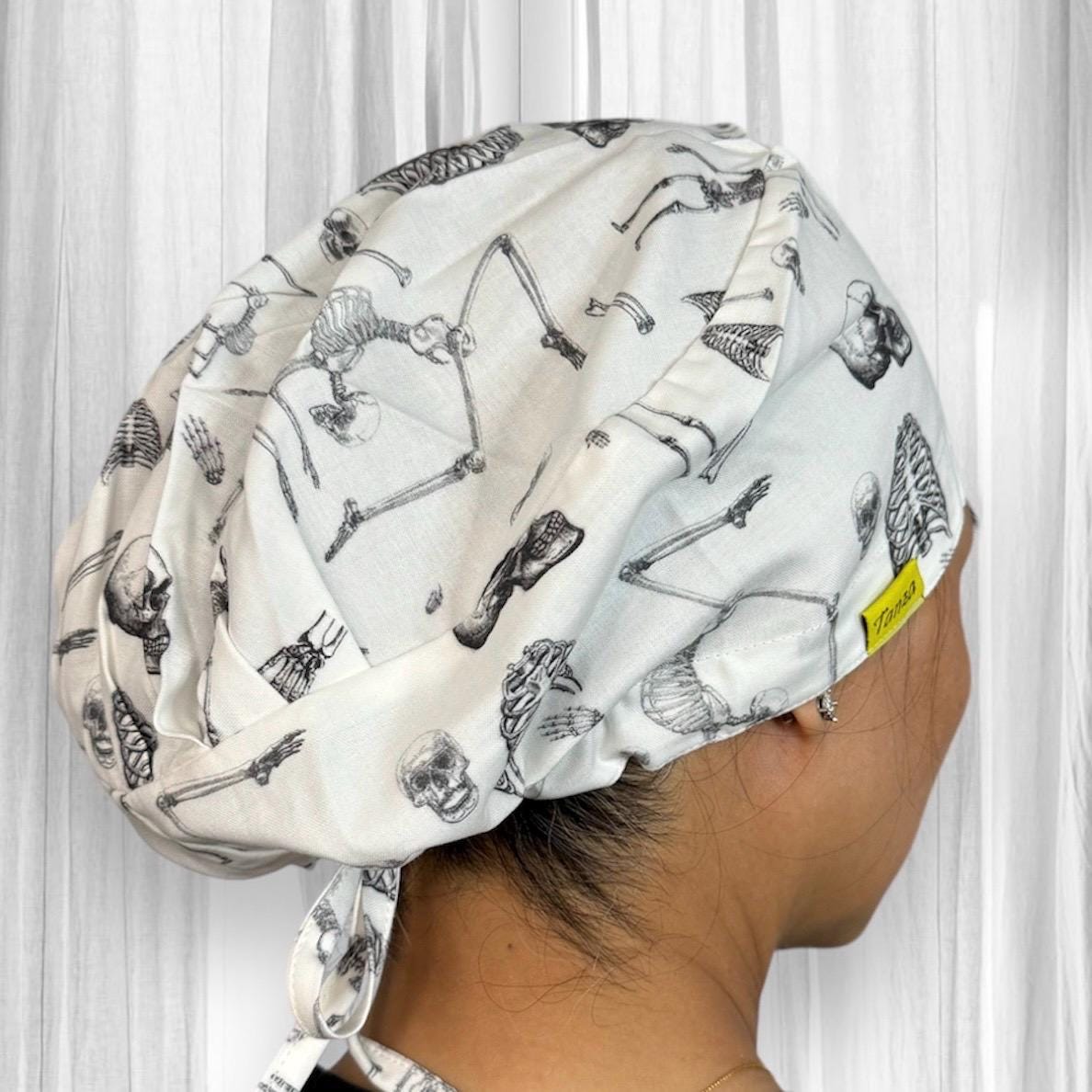 A scrub cap featuring a pattern of anatomical skeleton drawings in black on a white background.