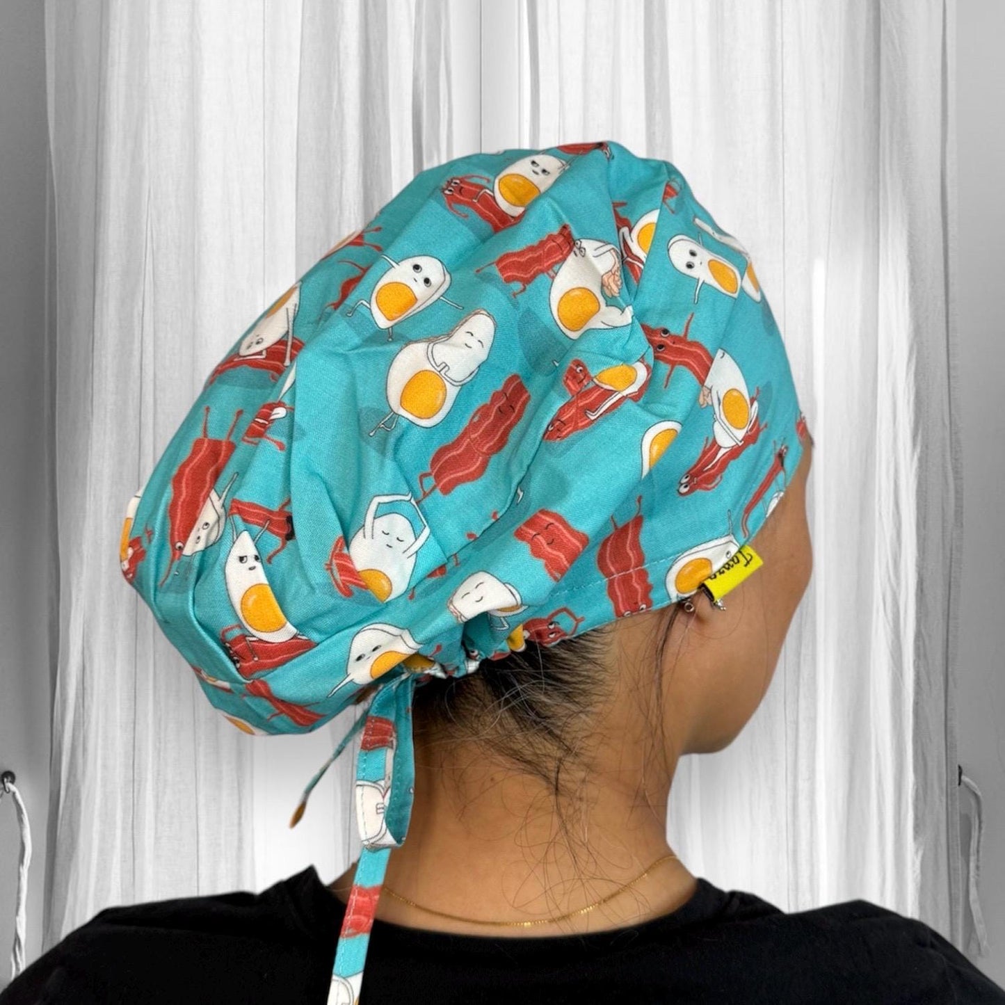 A colorful cap adorned with playful illustrations of eggs and bacon on a teal background.
