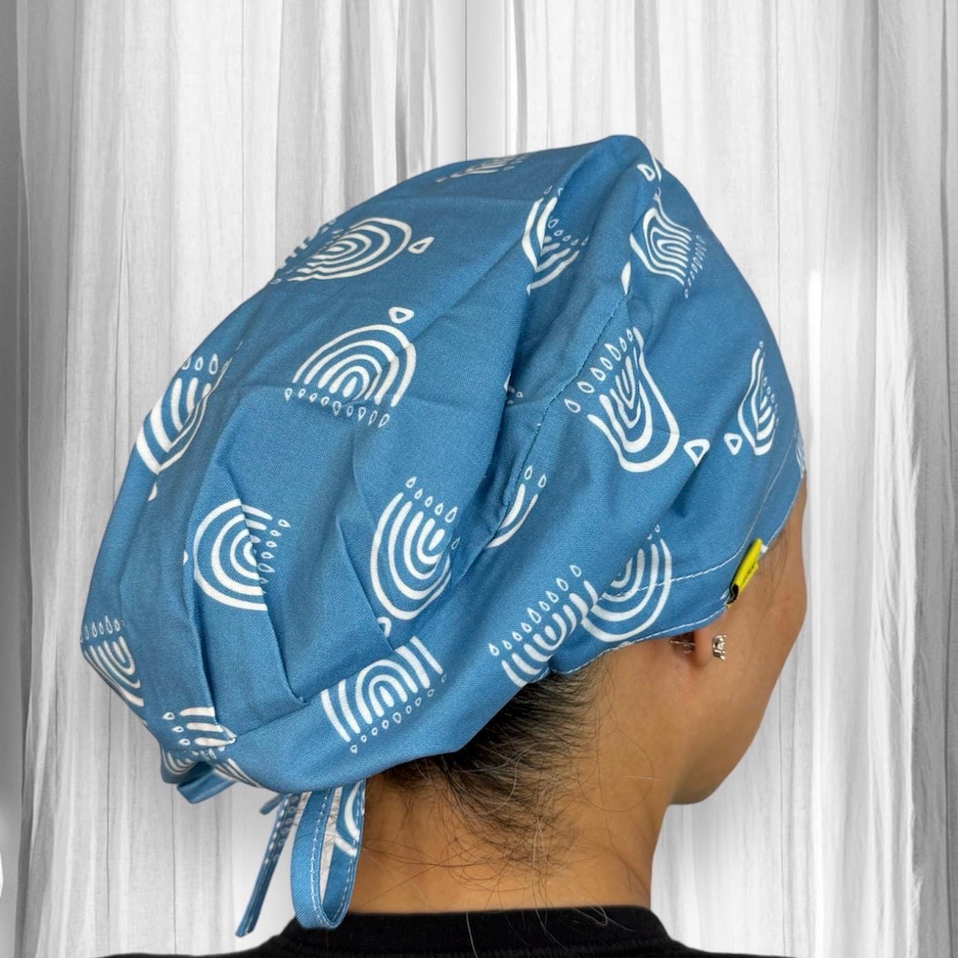 A person wearing a blue scrub cap with white abstract patterns, featuring geometric shapes and lines, tied at the back.