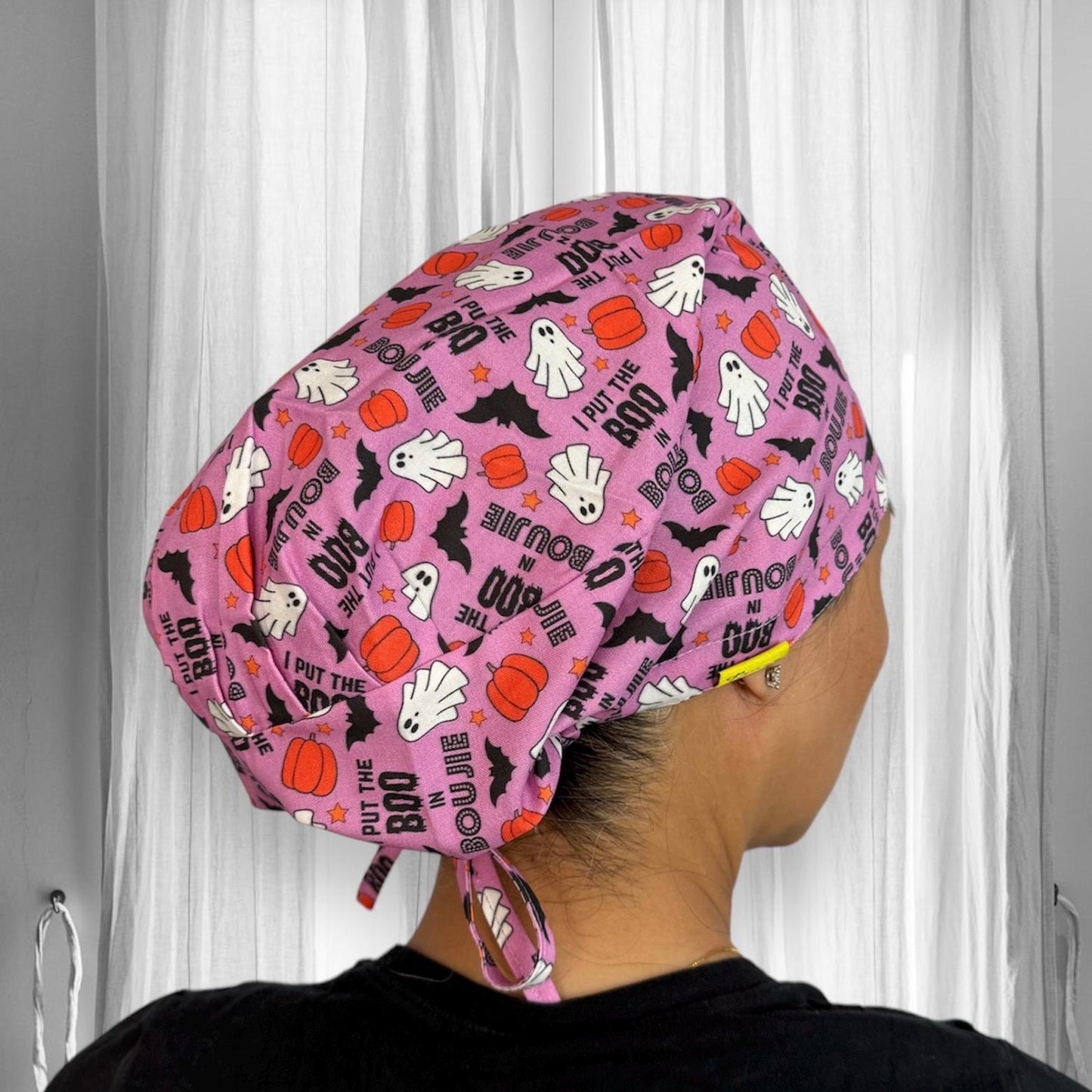 A colorful scrub cap featuring a playful Halloween-themed pattern with white ghosts, orange pumpkins, black bats, and text that reads "I put the BOO in boujie."