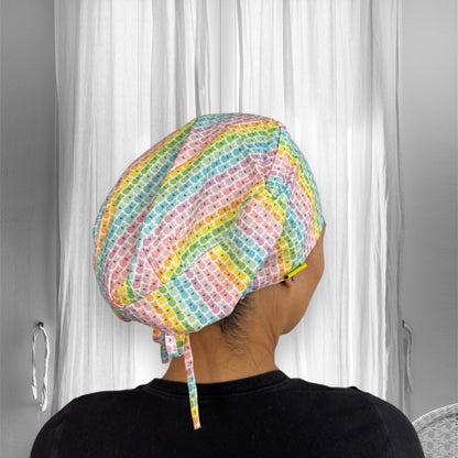 A person wearing a colorful patterned scrub cap with pastel shades of pink, blue, green, yellow, and orange, featuring a tie at the back. 
