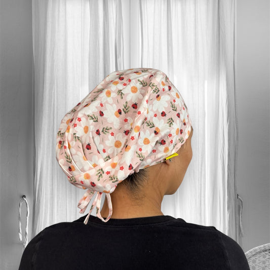 A person wearing a floral-patterned scrub cap. The cap features a design of white flowers with yellow centers and small red accents.
