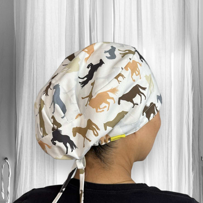 A person wearing a scrub cap. The cap is predominantly white with a pattern of various horse silhouettes in different colours such as black, brown, tan, and grey. The horses are depicted in different poses, like running, standing, and rearing. 