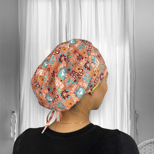 A person wearing a colorful scrub cap with a vibrant, playful design. The cap features patterns of flowers, retro vans. The dominant colors are shades of orange, blue, yellow, and red.