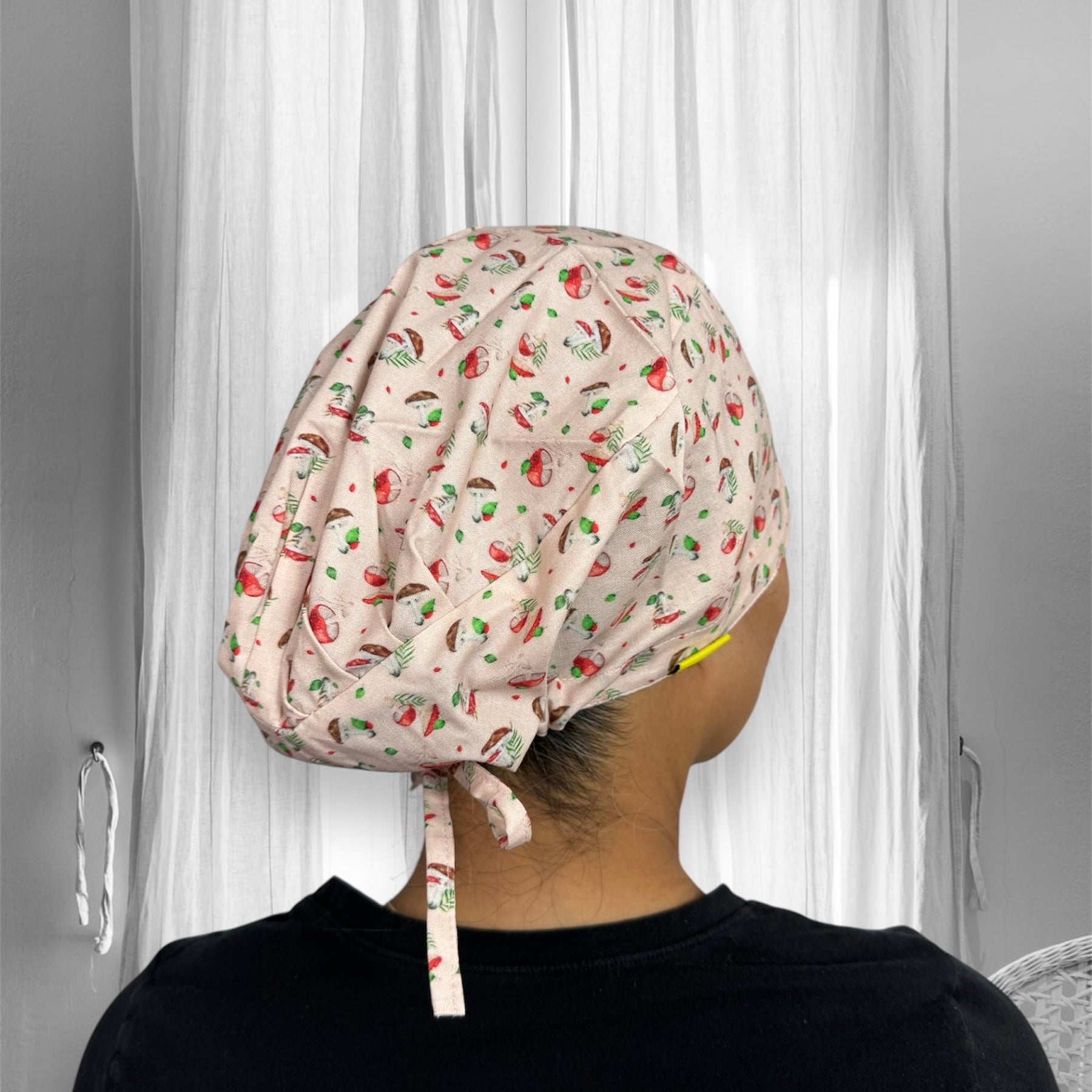 A person wearing a scrub cap with a playful pattern featuring small illustrations of mushrooms and leaves. The cap is tied at the back.