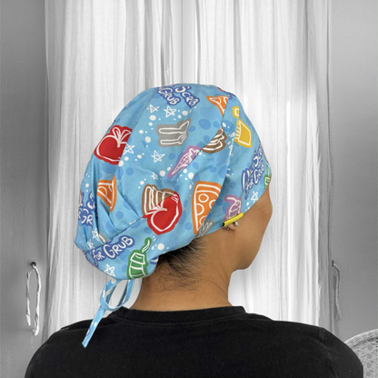 A person wearing a brightly colored scrub cap. The cap is blue with playful, vibrant illustrations featuring various food items like pizza slices, ice cream cones, cupcakes, apples, and drinks. The words "Scrub for Grub" are visible as part of the design.