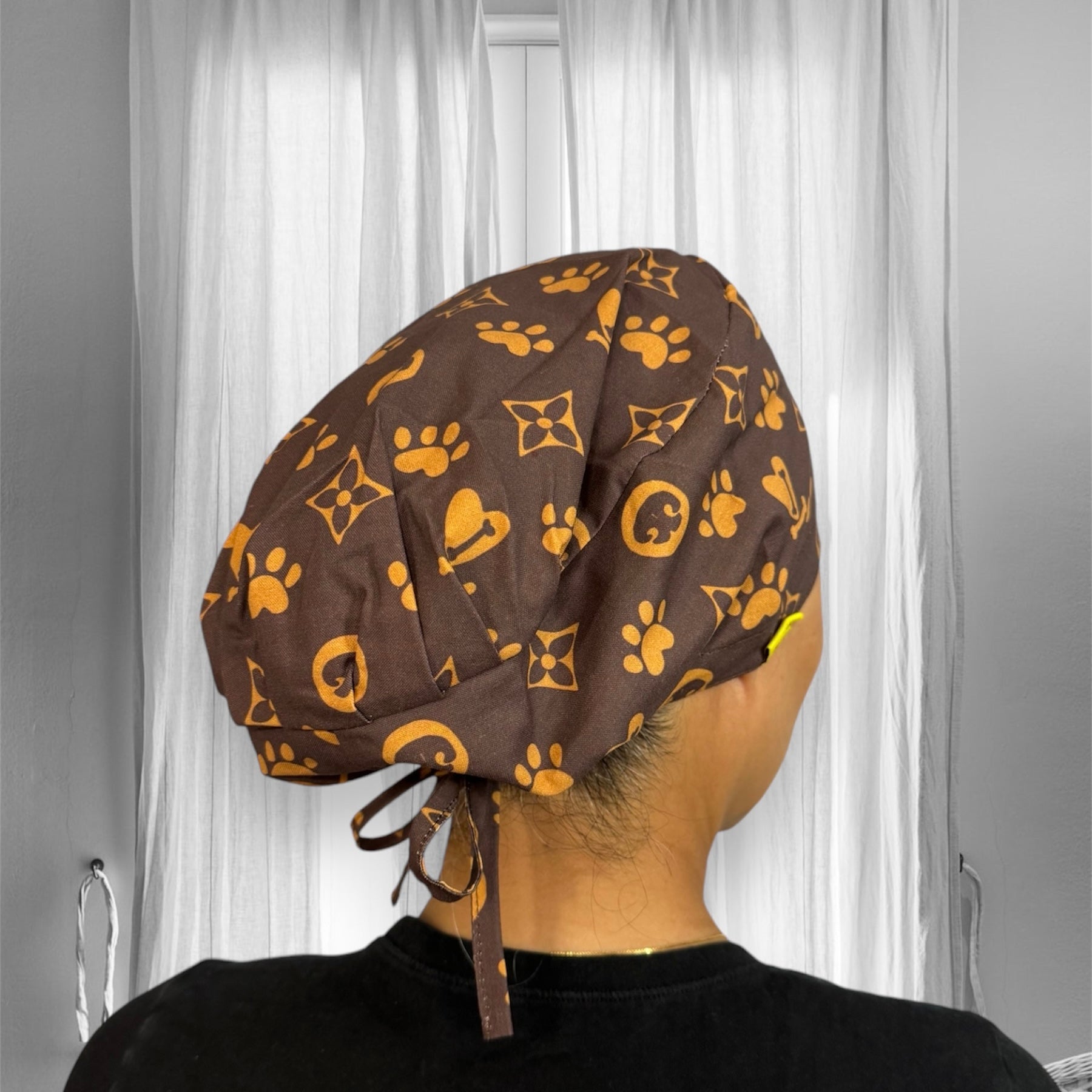 A brown scrub cap with a pattern featuring paw prints and floral designs in yellow.
