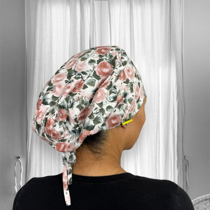 A floral-patterned scrub cap with pink roses and green leaves on a white background.