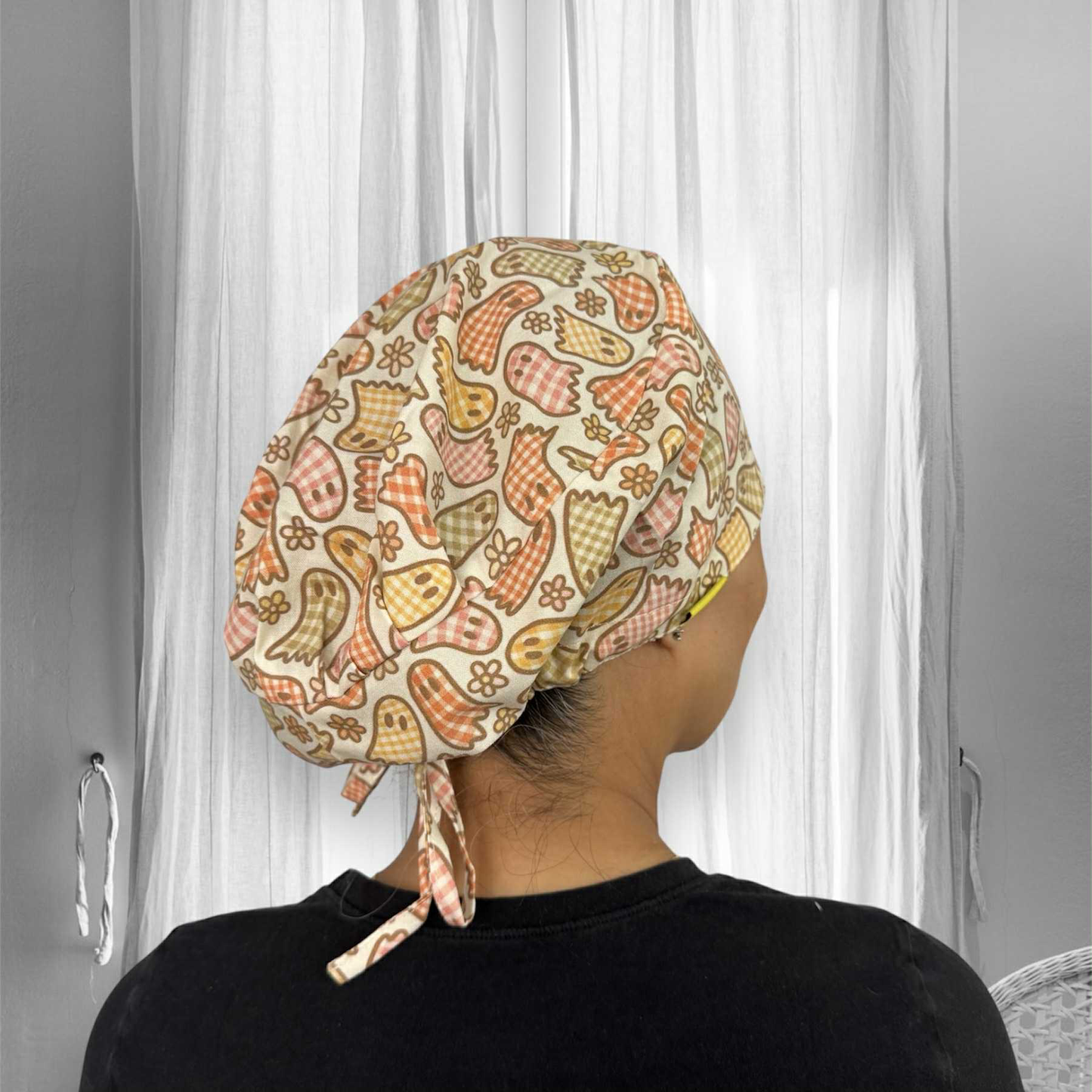 A person wearing a scrub cap with a colorful ghost and floral pattern. The cap features shades of orange, yellow, and bronze, with the birds designed in checkered style.