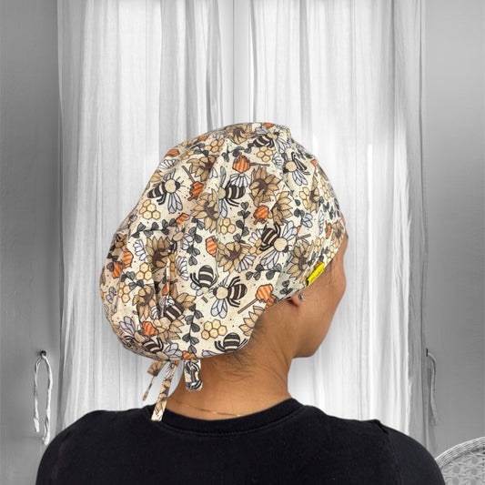 A person wearing a colorful scrub cap with a pattern of bees and flowers. The cap features various shades of orange, yellow, and black.