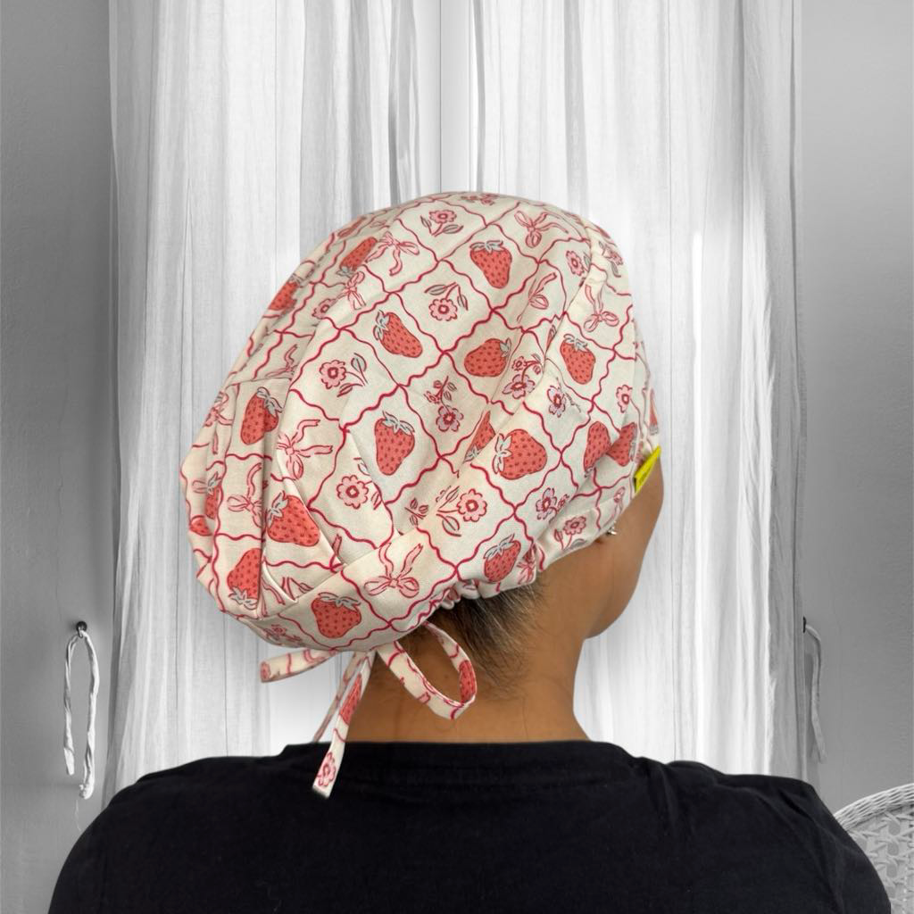 A person wearing a light-colored fabric cap with red strawberry and floral patterns arranged in a checkered design. 