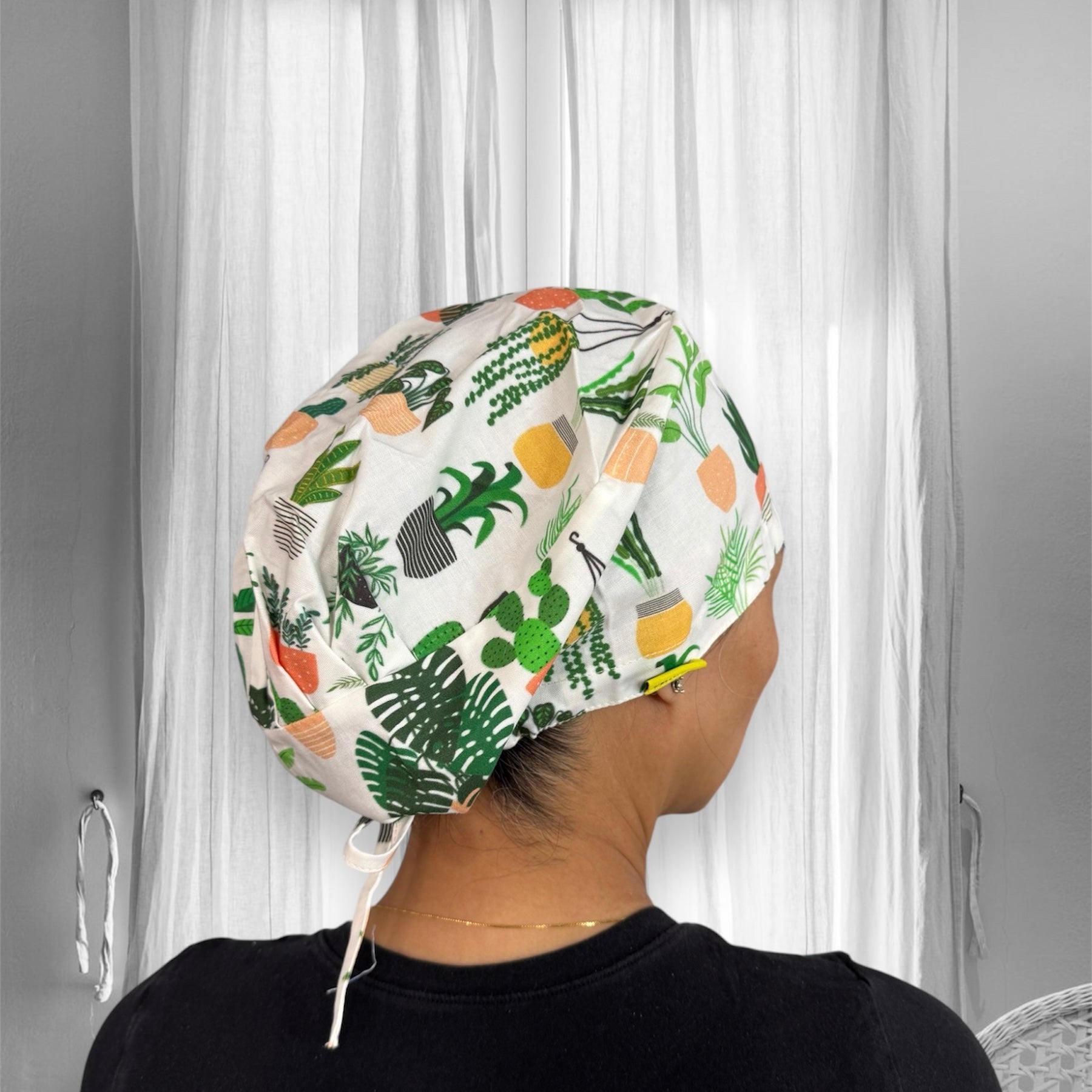 A scrub cap with a vibrant plant pot pattern. The scrub cap, adorned with various green and orange potted plant designs.