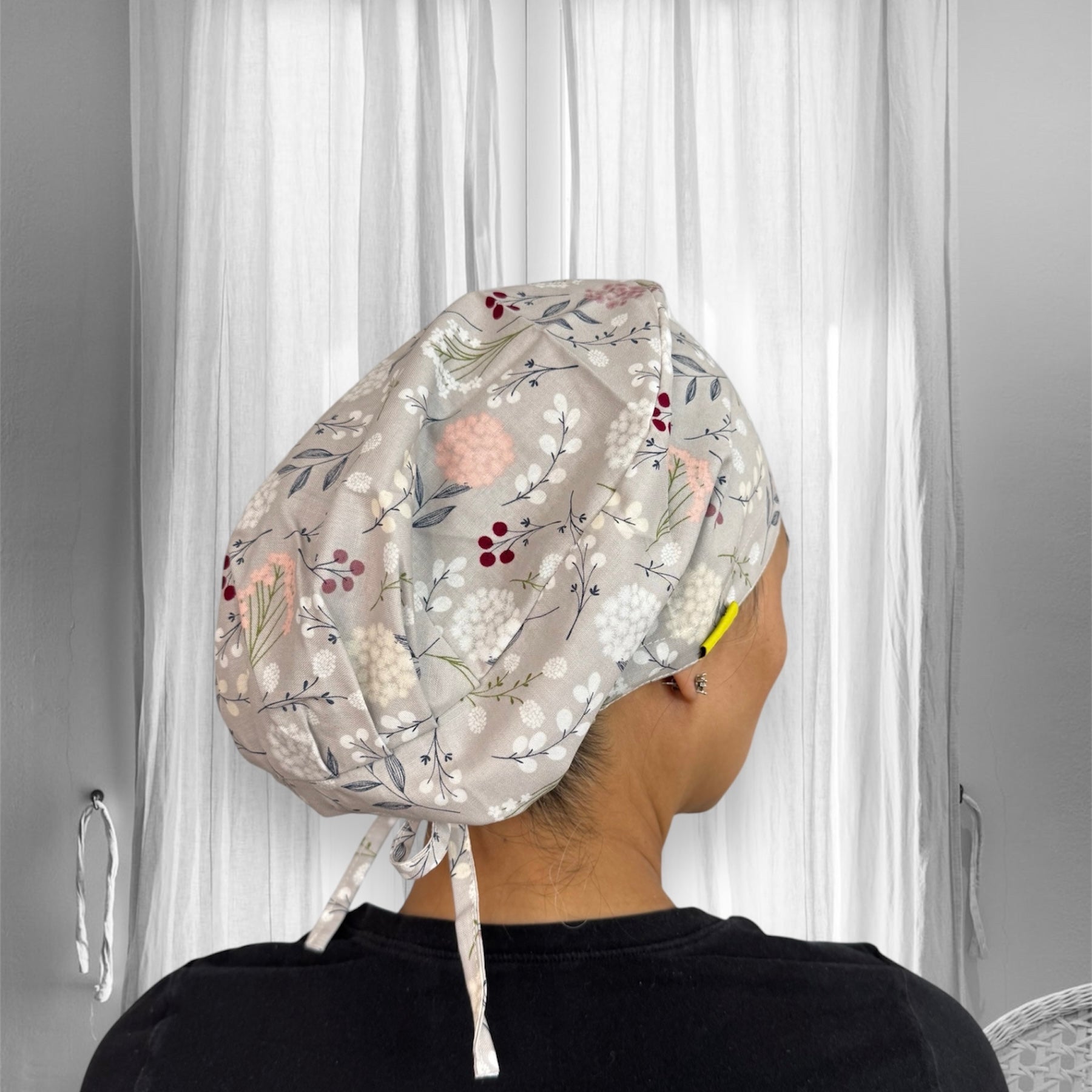 A floral-patterned scrub cap with pastel colors, featuring delicate flowers and berries on a light grey fabric. 