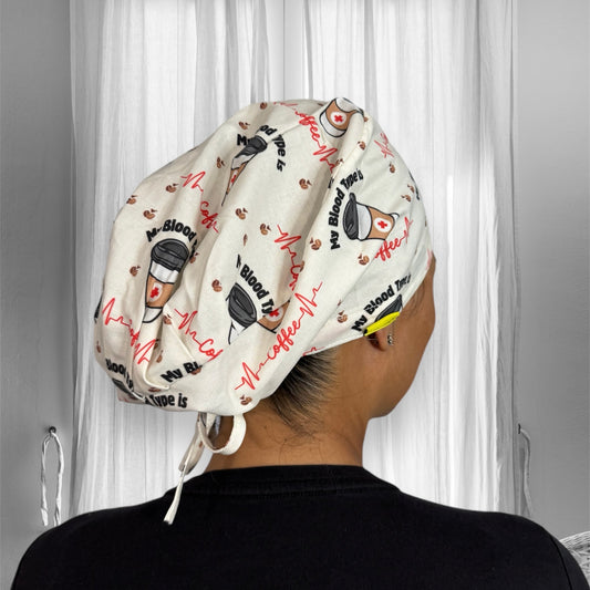 A person wearing a white scrub cap with playful designs, featuring illustrations of coffee cups, coffee beans, and text that reads "My Blood Type is Coffee," set against a subtle background of medical symbols and an EKG line. 