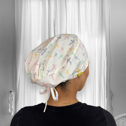 A person wearing a scrub cap with a pattern of pastel-colored crosses.