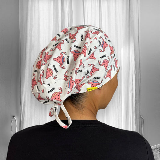 A person wearing a scrub cap featuring a playful pattern of cartoon uterus illustrations with the word "Push!" printed repeatedly.