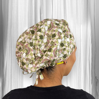 A person  wearing a scrub cap with a pattern of rainbows, clovers, and the word "LUCKY" printed on it. The cap is in shades of green and white, tied at the back.