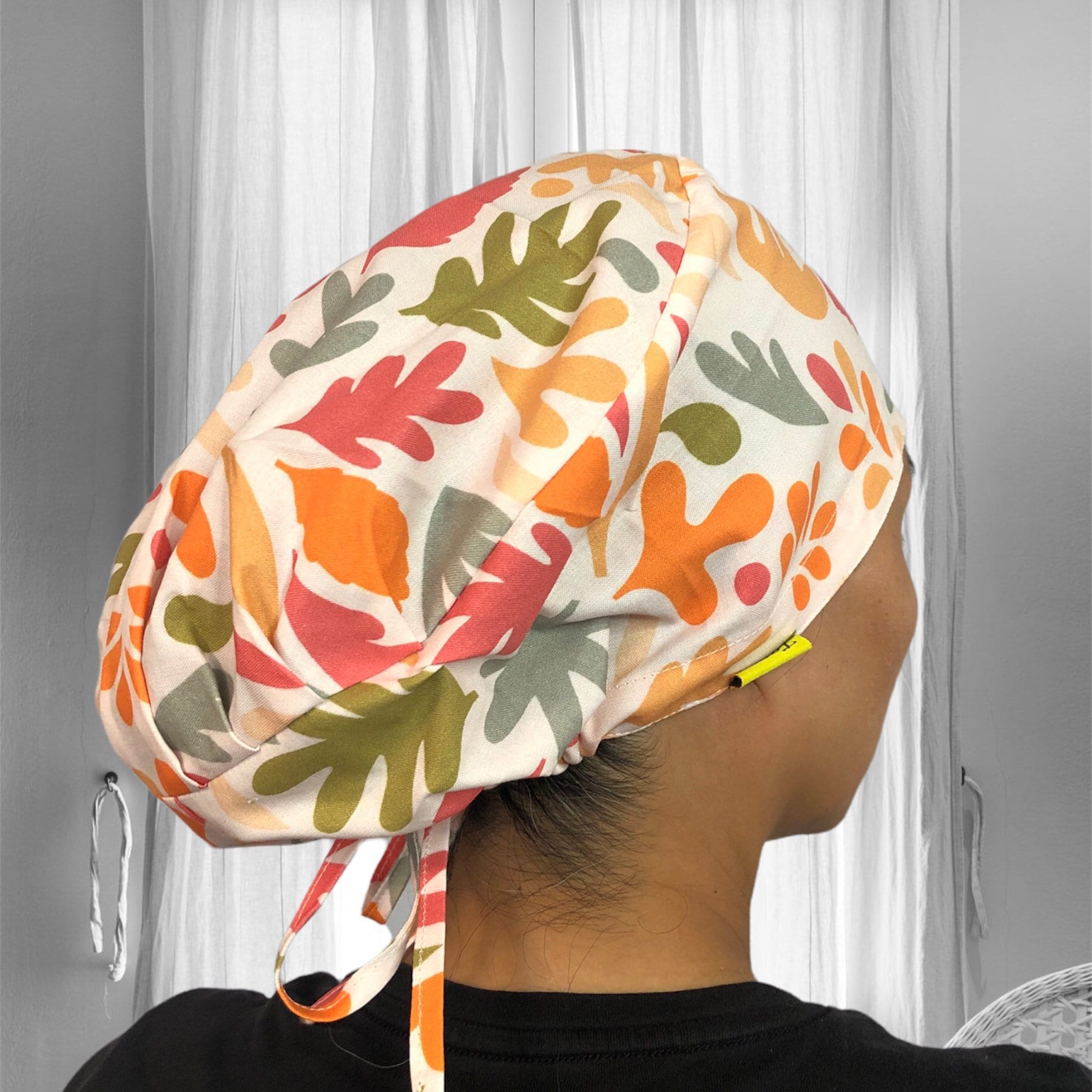 A colorful scrub cap with abstract leaf patterns in shades of orange, green, and pink.