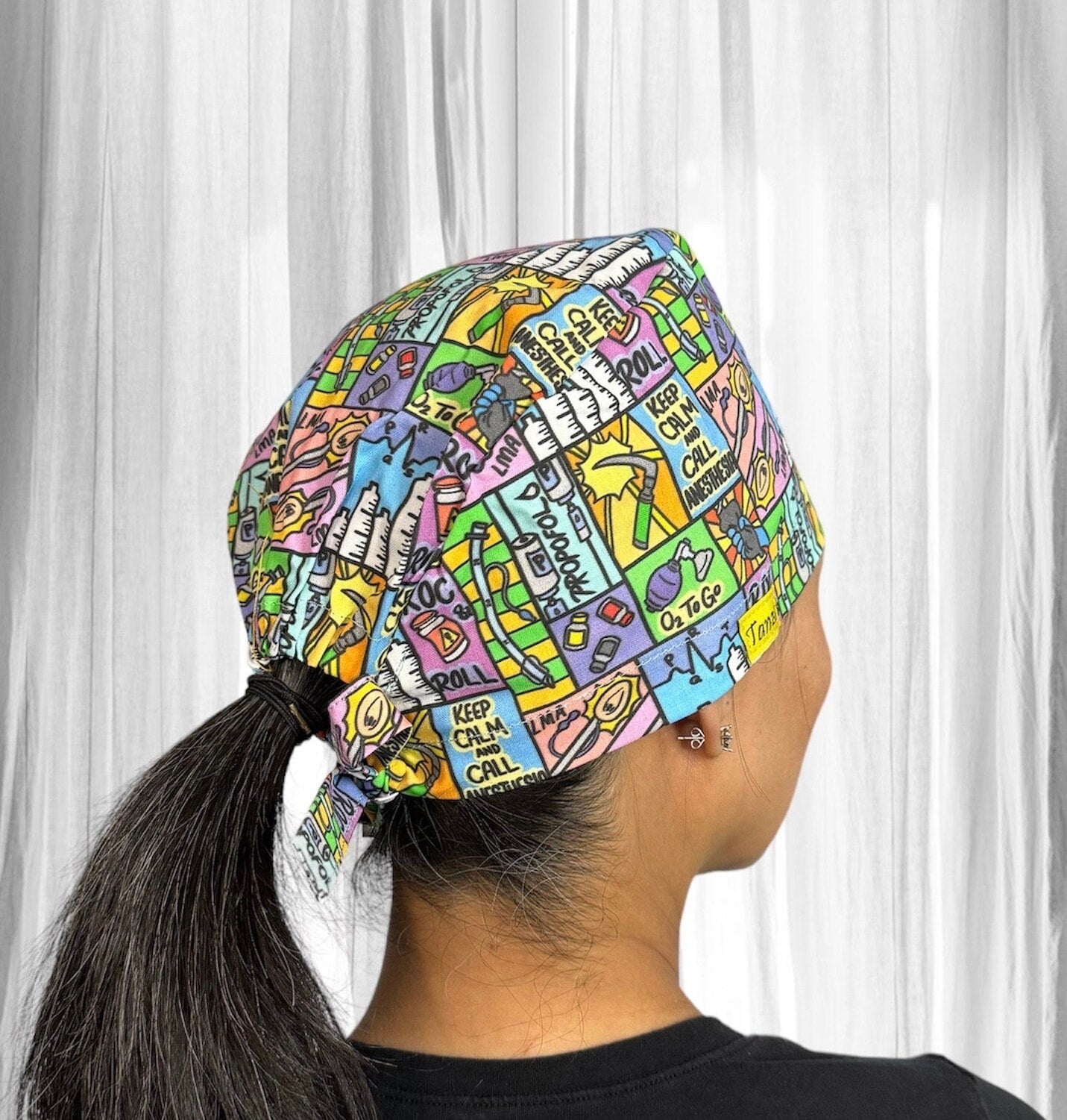 A colorful scrub cap featuring a vibrant pattern of illustrated phrases and objects.